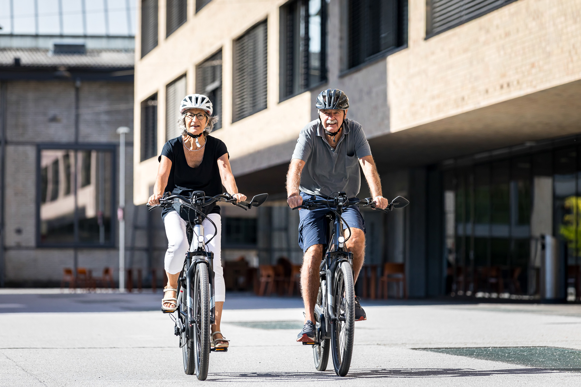 Zwei ältere Menschen fahren E-Bike in urbaner Umgebung mit Solarvignette